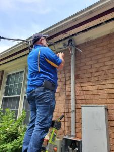 A GB Electrical technician is on a latter outside a brick home repairing the powerline going into the house. The power line was damaged during a storm. 